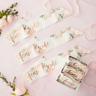 Set of six white paper sashes with floral design and rose gold 'Team Bride' lettering, featuring pink ribbon tiesâ€”ideal for hen party celebrations.