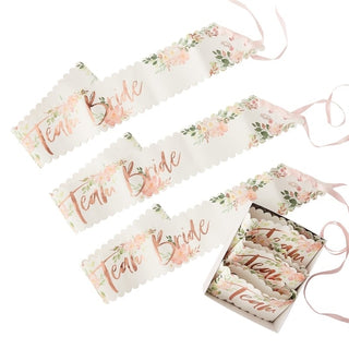 Set of six white paper sashes with floral design and rose gold 'Team Bride' lettering, featuring pink ribbon tiesâ€”ideal for hen party celebrations.