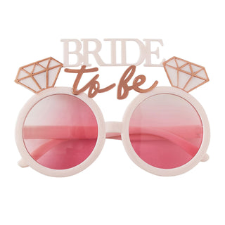 Blush pink sunglasses with rose gold 'Bride To Be' lettering and diamond accents, ideal for hen party celebrations.