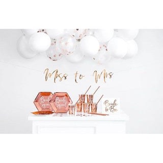 Rose gold hen party decoration set with balloons, banners, and confetti displayed on a wall