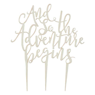 Wooden cake topper featuring the phrase "And So The Adventure Begins" in elegant script, measuring 22cm x 15cm, ideal for wedding or engagement cakes.